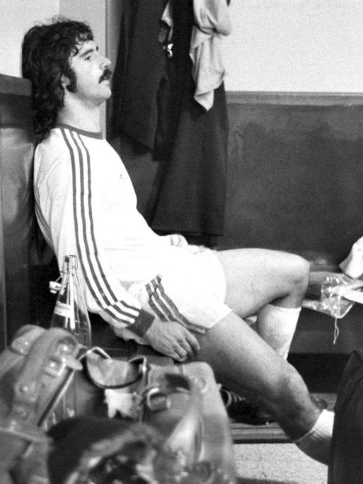 Gerd Müller sitzt hinten links auf einer Bank in der Kabine. Er wirkt völlig erschöpft nach einem Fußballspiel.