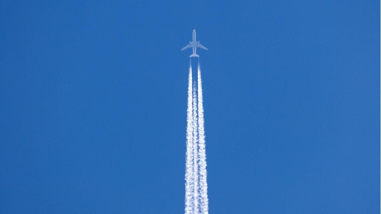 Flugzeug mit Kondensstreifen vor blauem Himmel