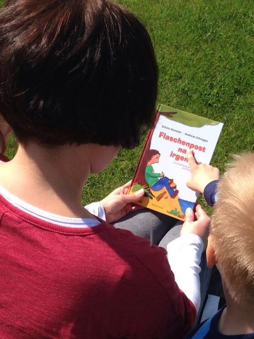 Eine Mutter sitzt mit ihren zwei Kindern auf einer Bank und hält ein Buch in den Händen.