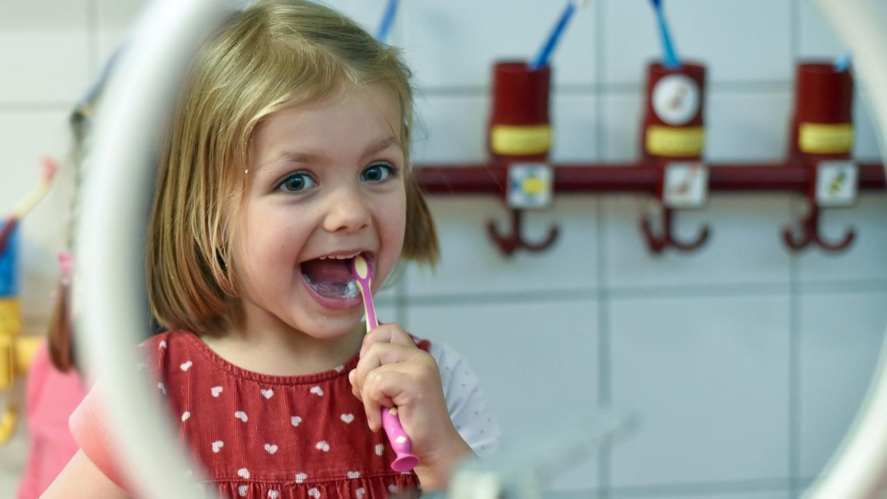 Ein Mädchen vom Kindergarten «Matroschka» in Frankfurt (Oder)(Brandenburg) steht am 25.06.2014 im Bad vor einem Spiegel und putzt ihre Zähne nach dem Mittagessen.