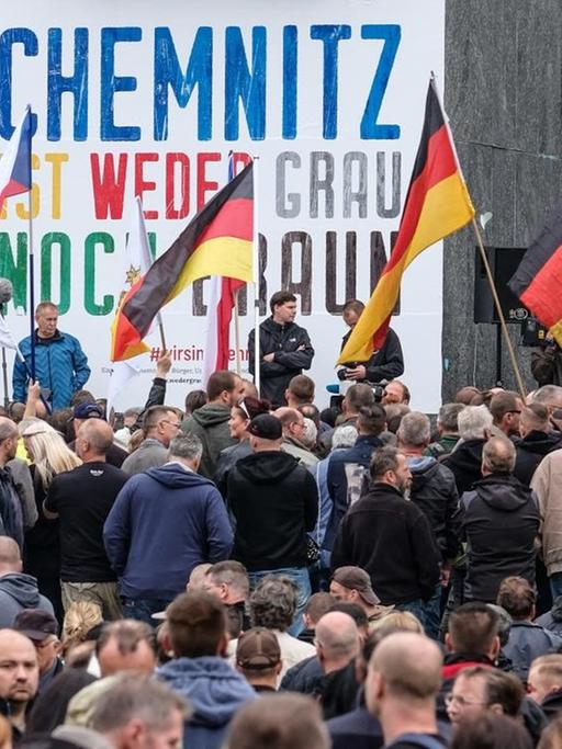 Demonstranten stehen in Chemnitz vor der Karl-Marx-Statue. Darauf ein Spruchband: "Chemnitz ist weder grau noch braun."