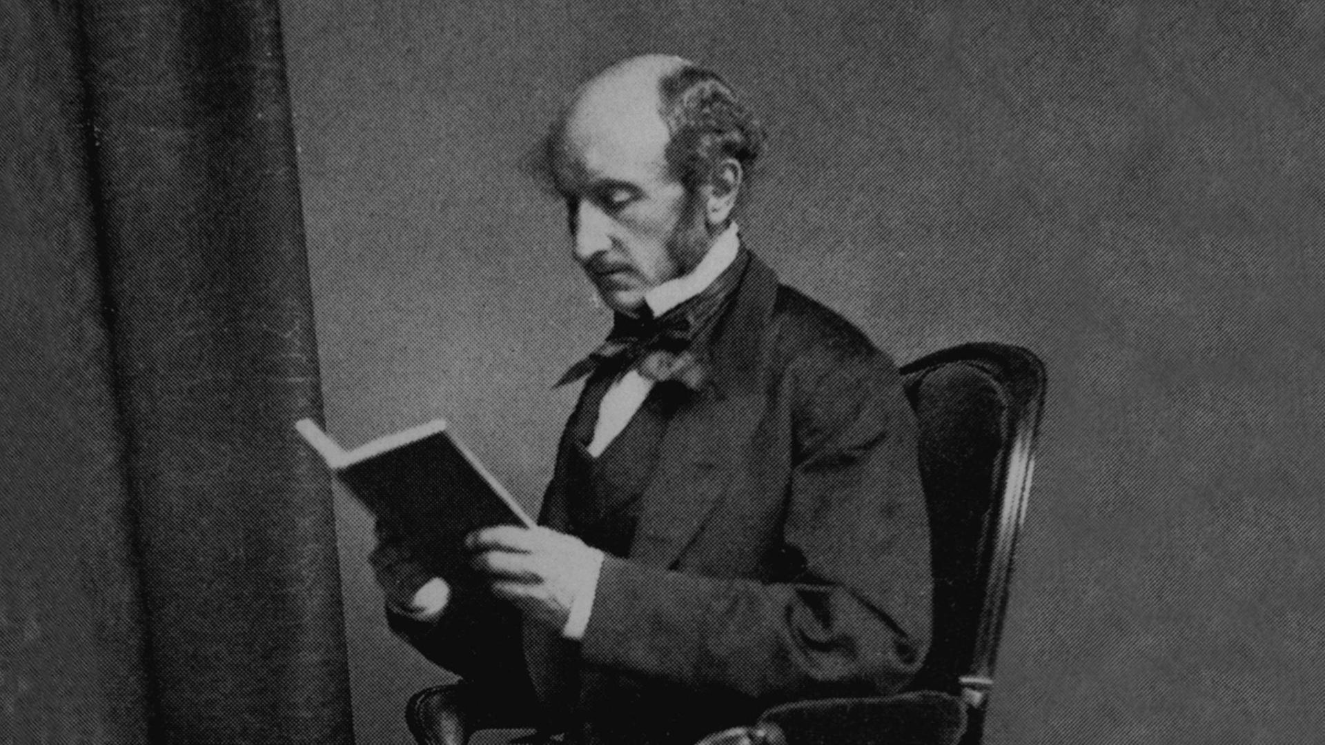 Porträt von John Stuart Mill (1806–1873). Er sitzt in einem Stuhl in liest ein Buch.