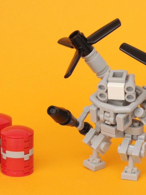 Lego-Roboter mit Propellern neben drei kleinen, roten Fässern vor einem gelben Hintergrund