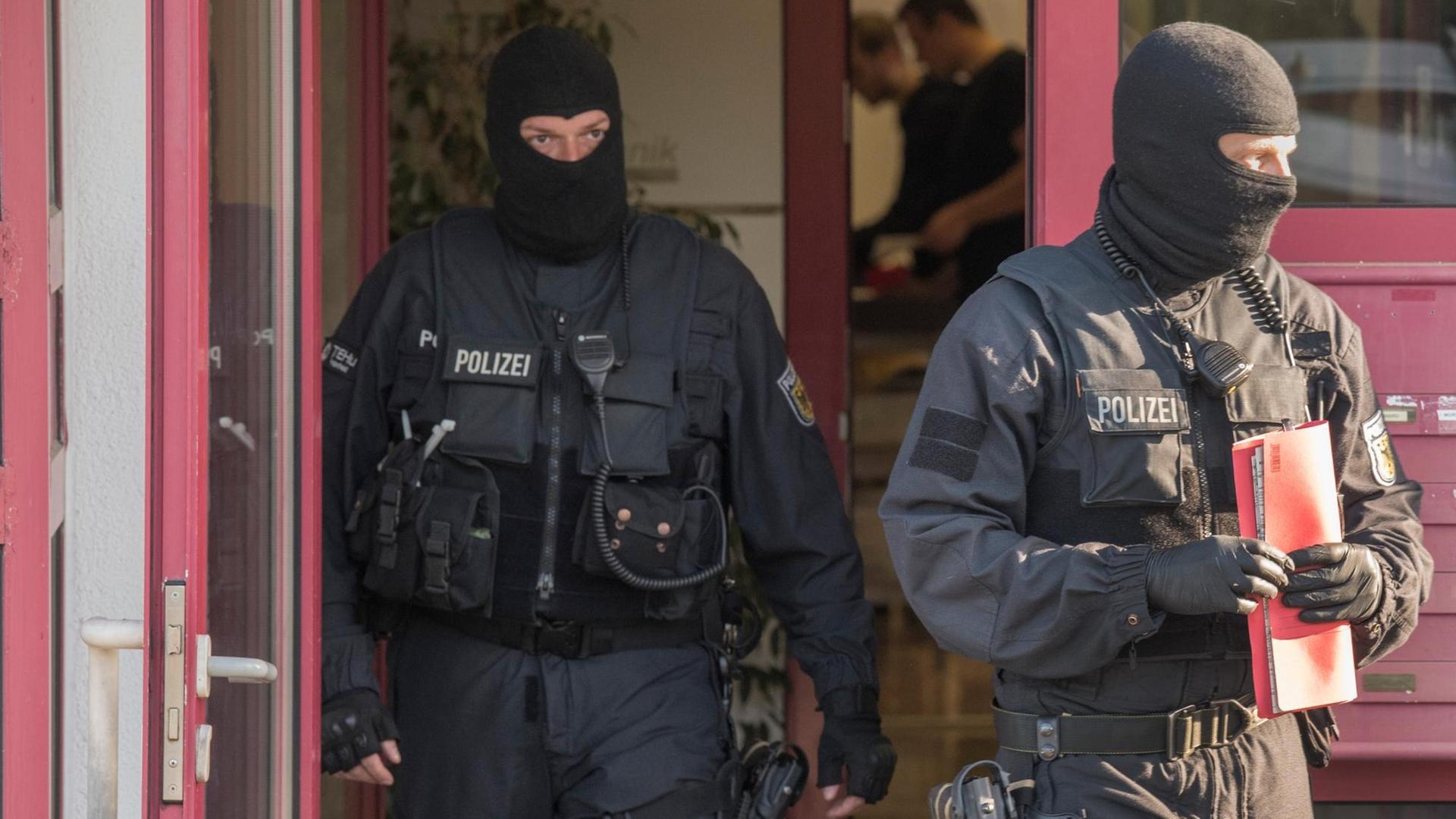 Zwei schwarz vermummte Polizisten treten aus der Tür des Bordells