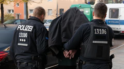 Bei einem Einsatz gegen arabischstämmige Clans in Berlin führen Polizeibeamte mit Handschellen einen festgenommenen Mann nach einer Razzia in einem Wohnhaus in Tempelhof ab. | Foto: Paul Zinken/dpa | Verwendung weltweit