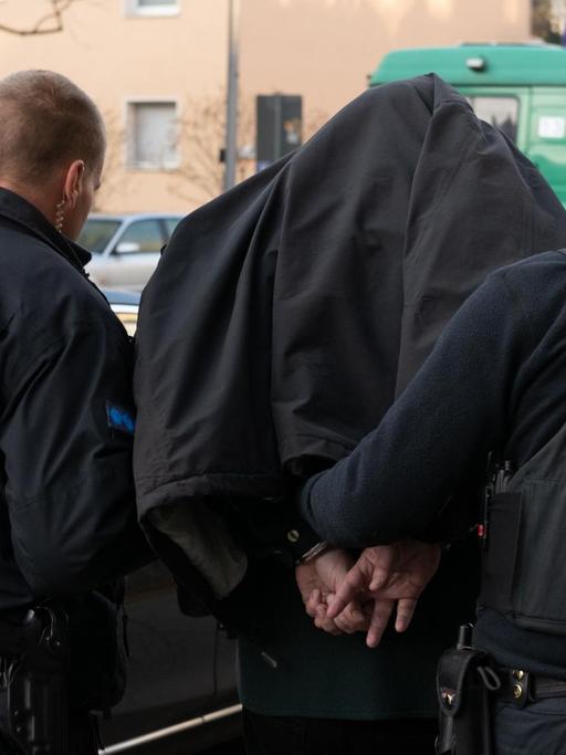 Bei einem Einsatz gegen arabischstämmige Clans in Berlin führen Polizeibeamte mit Handschellen einen festgenommenen Mann nach einer Razzia in einem Wohnhaus in Tempelhof ab. | Foto: Paul Zinken/dpa | Verwendung weltweit