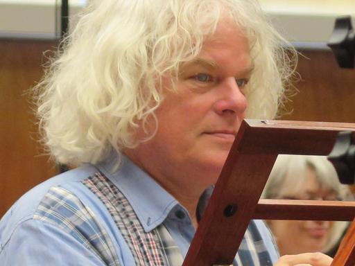 Ein älterer Mann mit mittellangen weißen Haaren sitzt in Seitenansicht vor einem Notenständer.