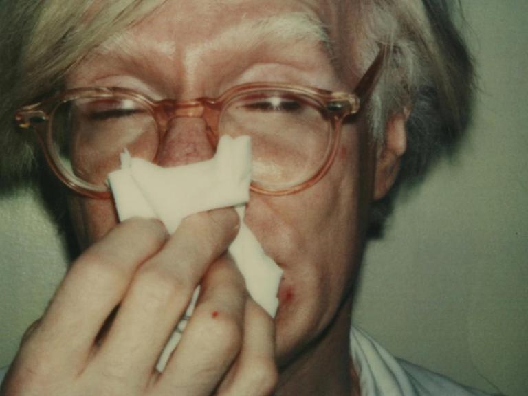 Das Bild zeigt ein Polaroid-Foto auf dem Andy Warhol sich die Nase putzt