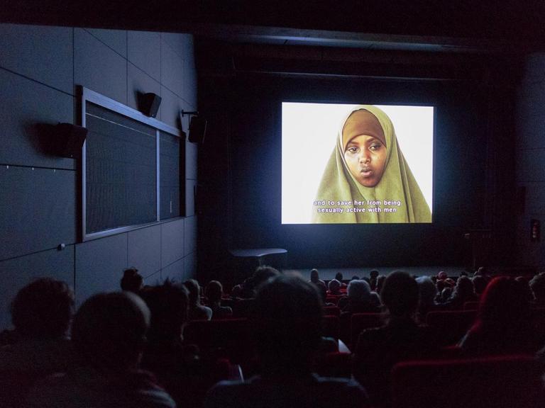 In einem dunklen Kinosaal schaut das Publikum auf die Leinwand - dort ist eine junge Frau mit Kopftuch zu sehen