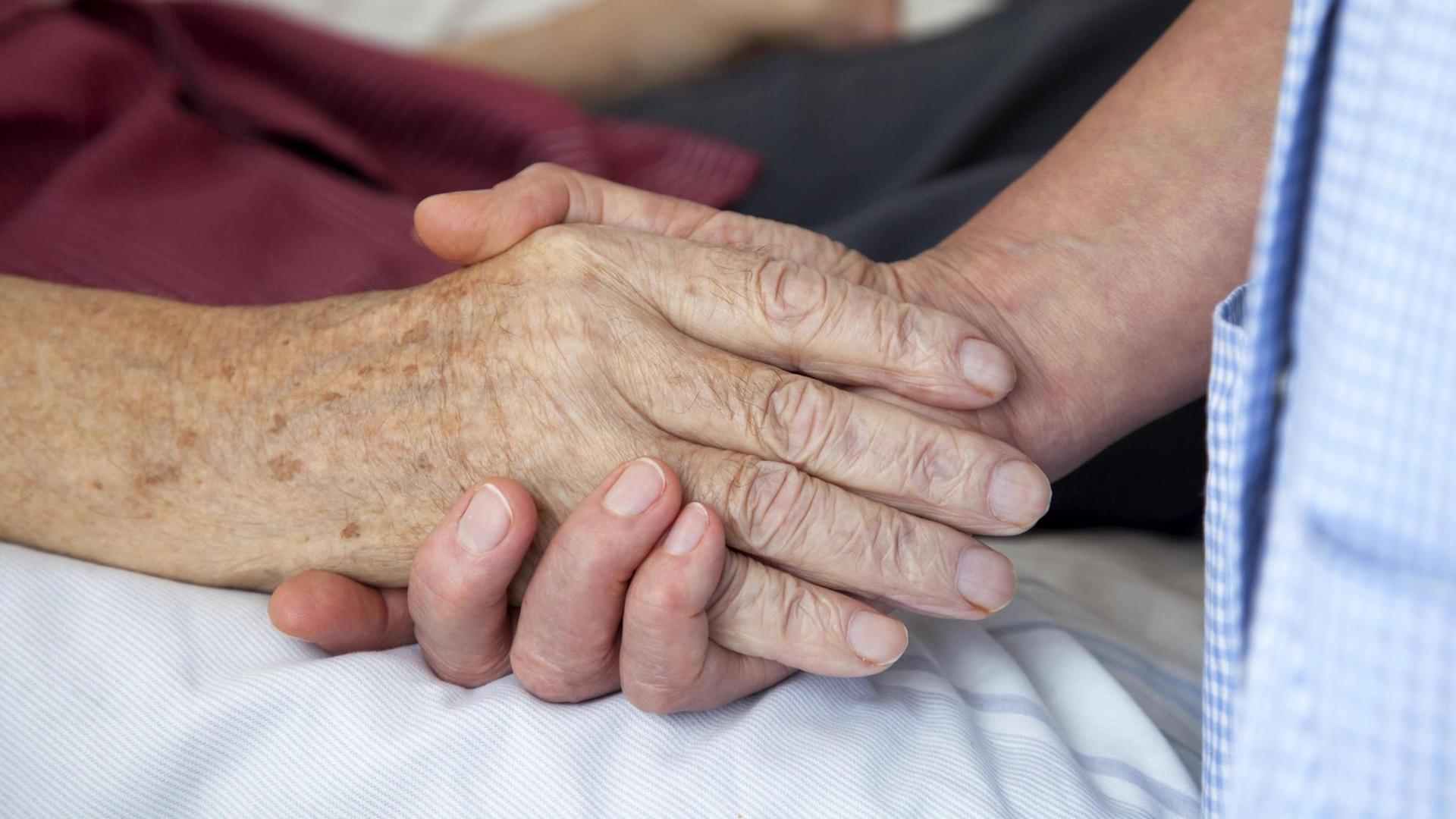 Die Hand einer Pflegerin hält die Hand eines Patienten.