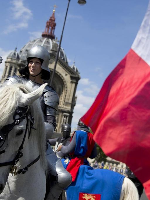 Eine Frau verkleidet als Jeanne d'Arc auf einem Pferd