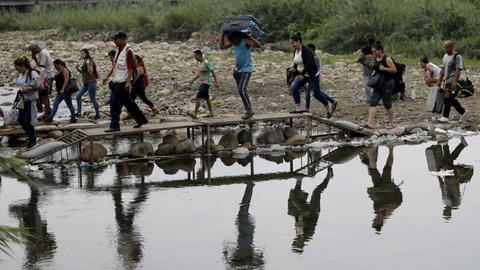 Männer, Frauen und Kinder gehen mit Gepäck an einem Fluss entlang