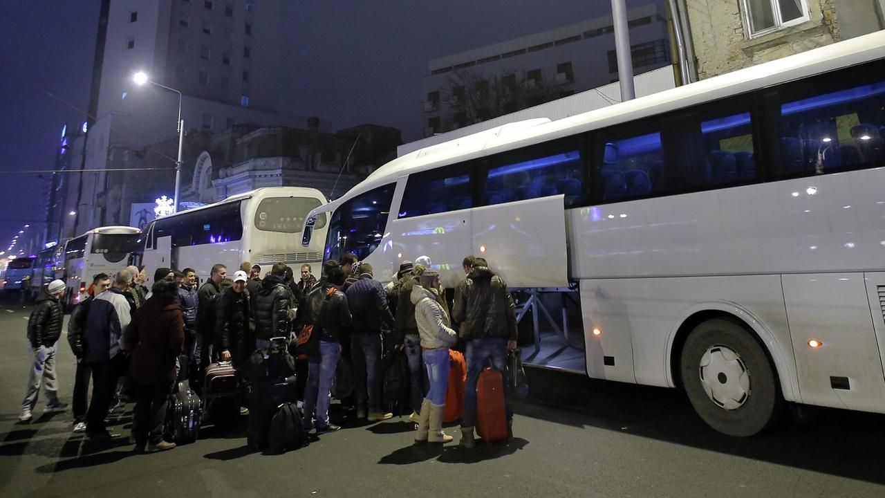 Rumänen warten vor einem Bus nach Deutschland und Belgien darauf, dass ihr Gepäck verladen wird.