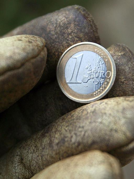 Eine Hand in einem Arbeitshandschuh hält eine Ein-Euro-Münze.