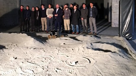 Mitarbeiter der Firma ispace stehen vor einem Sandfeld in einer Halle