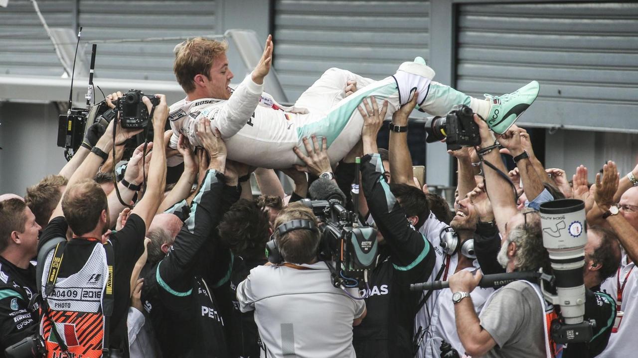 Die Techniker heben Rosberg im weißen Overall mit den Händen hoch, um ihn in die Luft zu werfen. Fotografen und Kameramänner dokumentieren die Szene. Die Techniker heben Rosberg im weißen Overall mit den Händen hoch, um ihn in die Luft zu werfen. Fotografen und Kameramänner dokumentieren die Szene.