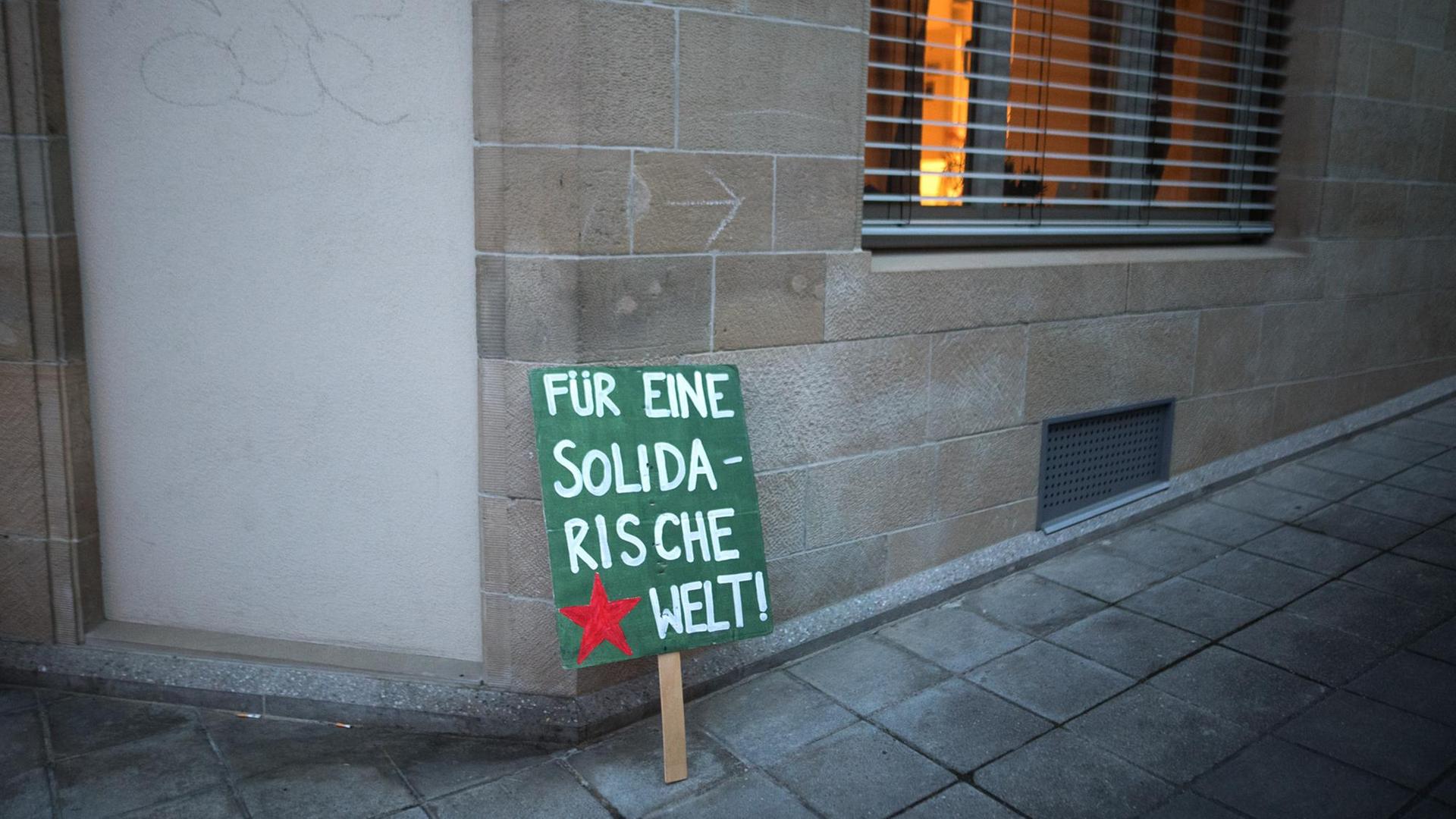 Ein Plakat mit der Aufschrift "Für eine solidarische Welt" steht nach einer Demonstration an eine Hauswand gelehnt.