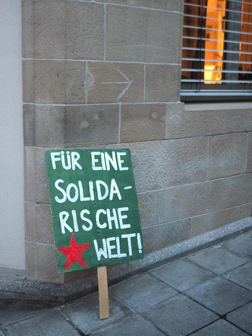 Ein Plakat mit der Aufschrift "Für eine solidarische Welt" steht nach einer Demonstration an eine Hauswand gelehnt.