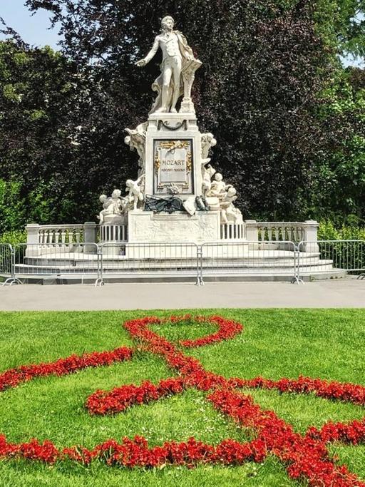 Blauer Himmel über dem Denkmal Mozarts im Park von Wien, vor dem aus roten Blumen ein Notenschlüssel gepflanzt wurde.
