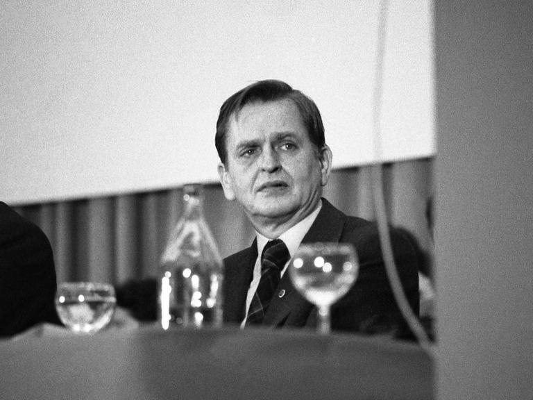 Olof Palme, bei einem Kongress am Tisch sitzend. Im Vordergrund Gläser.