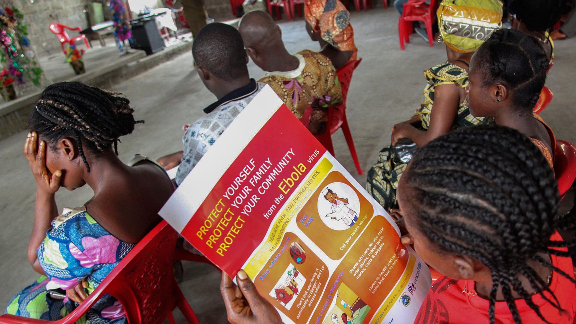 Frauen in Liberia sitzen auf Plastikstühlen und lesen Informationsblätter über den Schutz vor dem Ebola-Virus