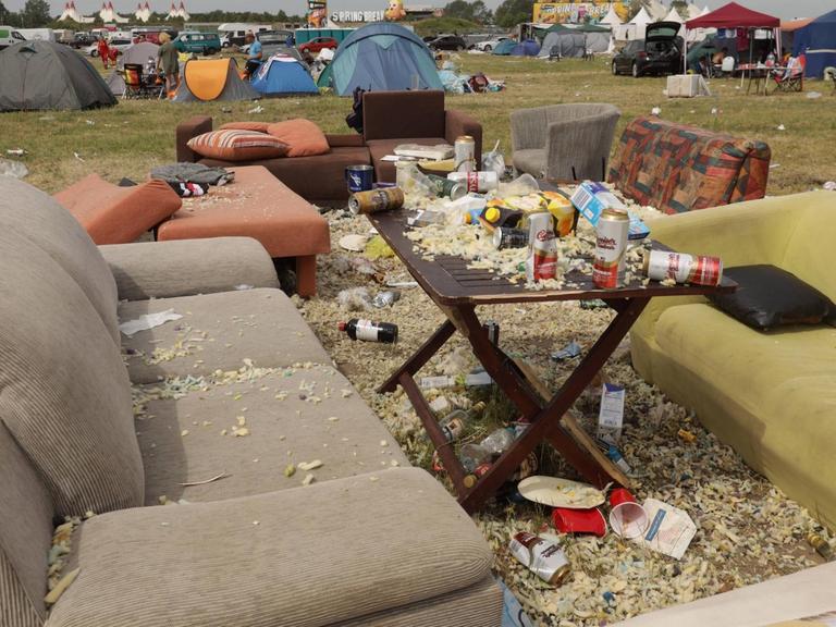 Das Bild zeigt eine vermüllte Campingwiese mit alten Sofas, die nach einem Rockfestival in Bitterfeld zurückgelassen wurden.