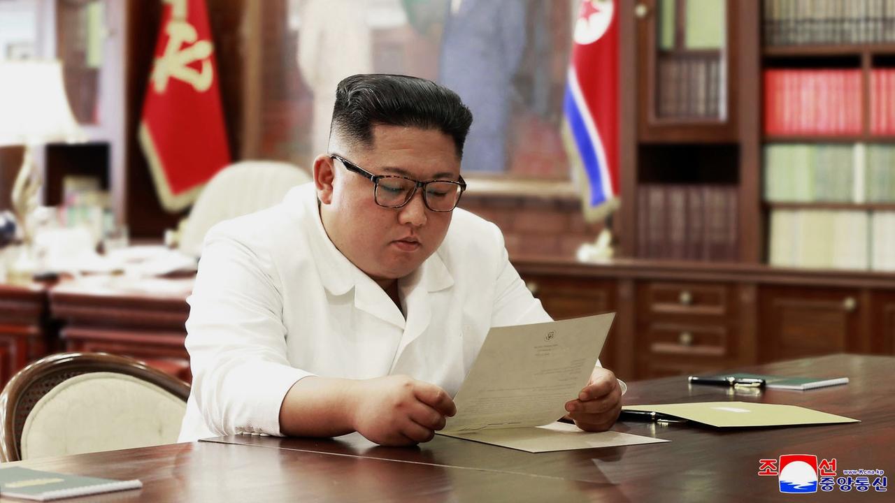 Kim sitzt im weißen Sakko in seinem Büro am Schreibtisch und liest den Brief.