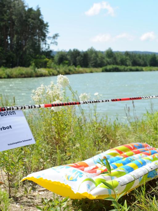 Ein Schild mit der Aufschrift "Betreten verboten Badeverbot" neben einer Luftmatratze an einem See.