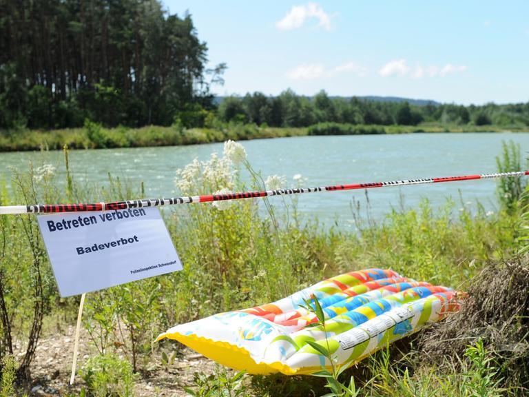 Ein Schild mit der Aufschrift "Betreten verboten Badeverbot" neben einer Luftmatratze an einem See.