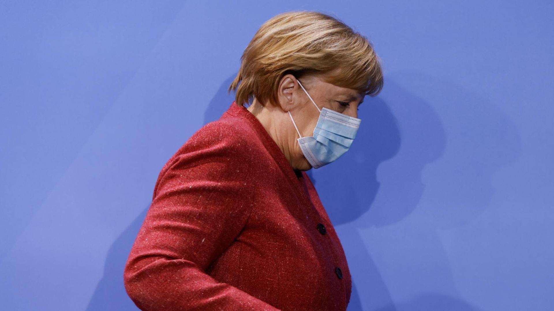 Bundeskanzlerin Angela Merkel (CDU) verlässt nach einer Pressekonferenz einen Saal im Bundeskanzleramt. Sie trägt einen roten Blazer und einen Mund-Nase-Schutz.