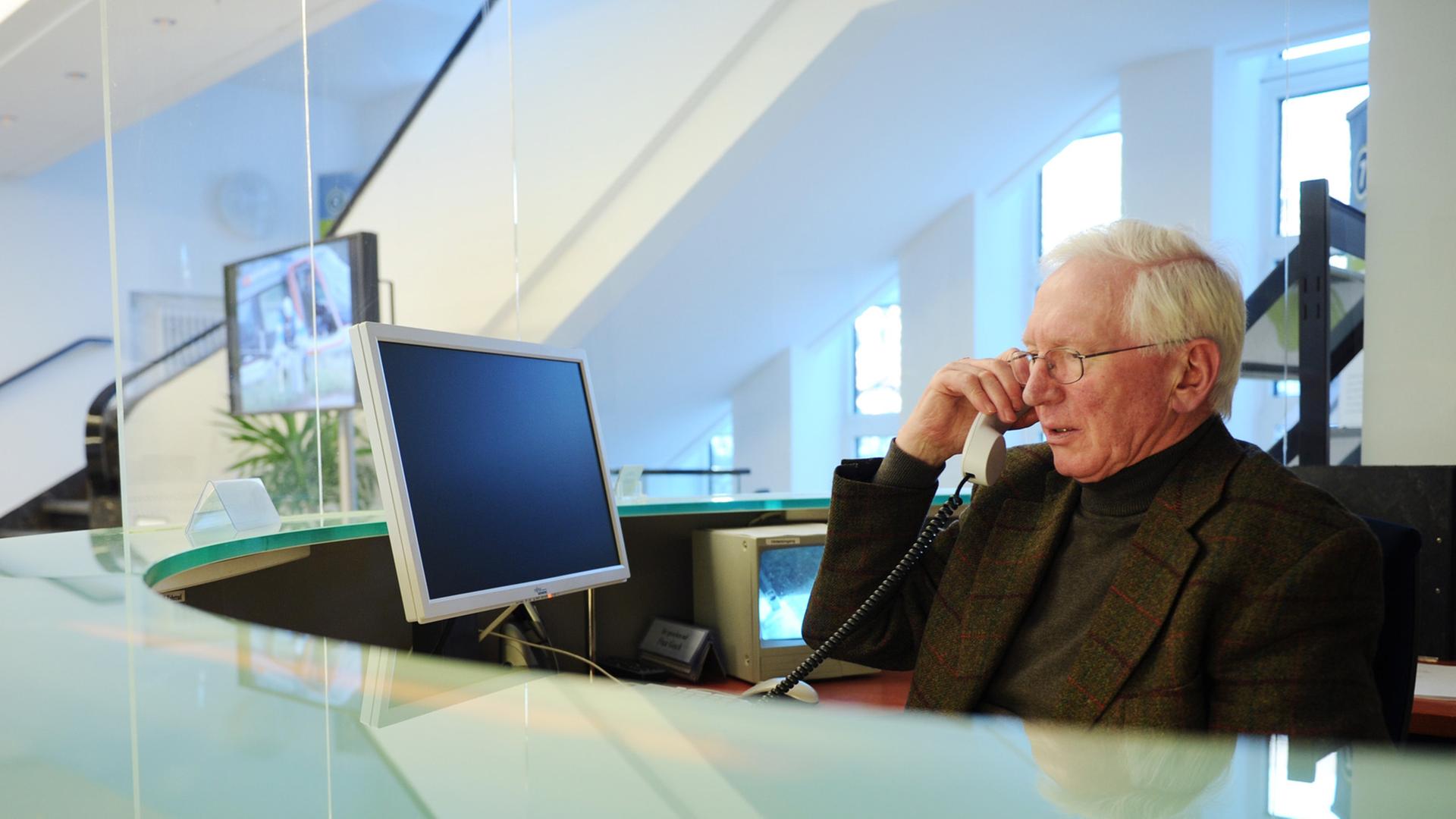 Ein Senior sitzt im Büro an einem Empfang und telefoniert.