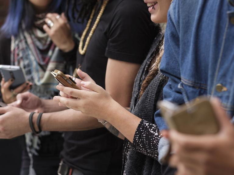Junge Menschen stehen zusammen und nutzen ihre Smartphones.