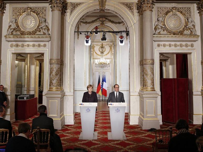 Bundeskanzlerin Merkel und Frankreichs Präsident Hollande stehen in einem prunkvollen Saal im Elysée-Palast in Paris an einem Stehpult.