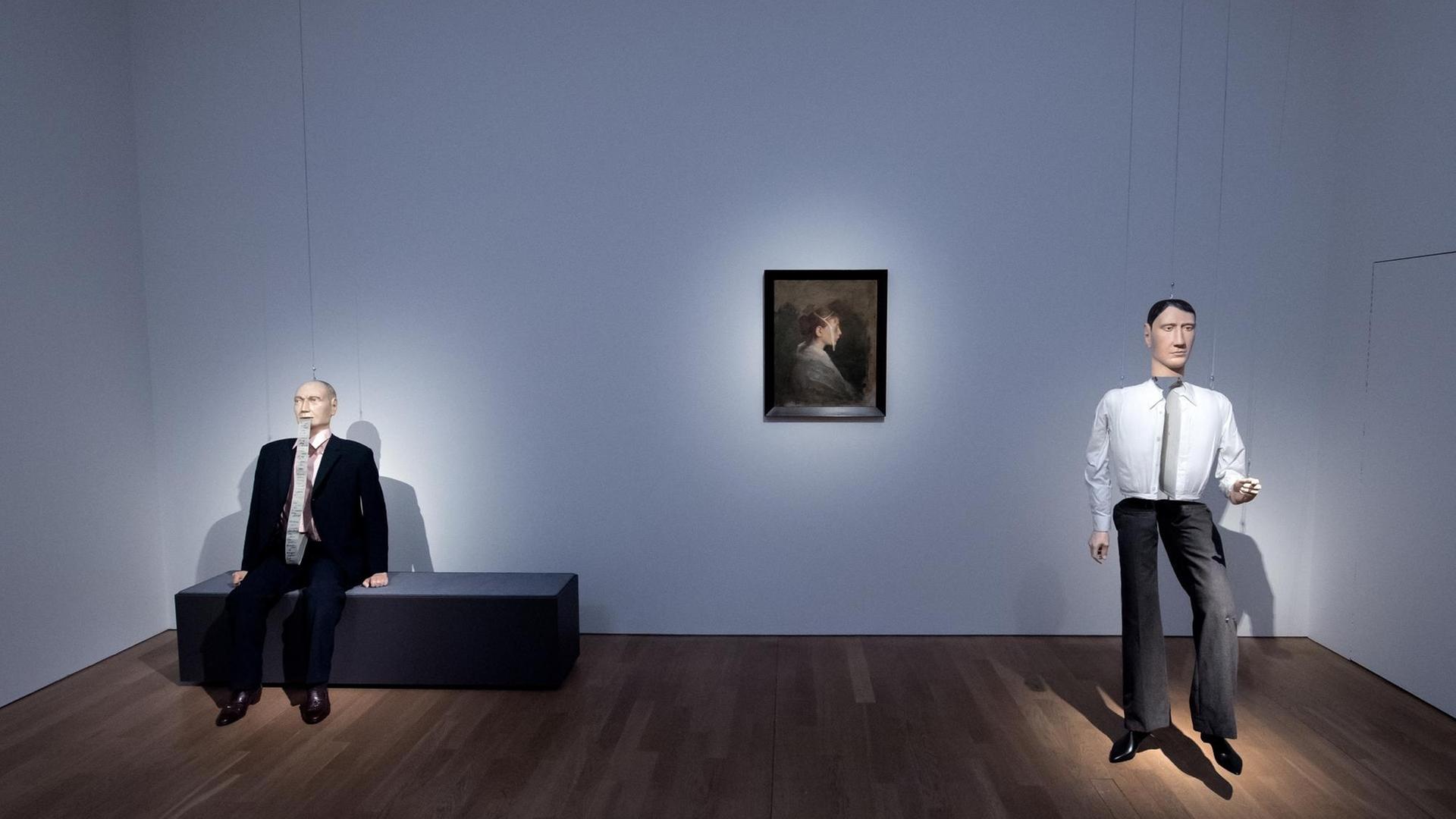 Die Installationen "Hans", "Kacia" und "Albert" des Künstlers Schinwald in der Kunsthalle München: Auf einer bank sitzt eine männliche Puppe, rechts davon hängt ein Porträtbild einer Frau, rechts davon steht eine männliche Puppe.