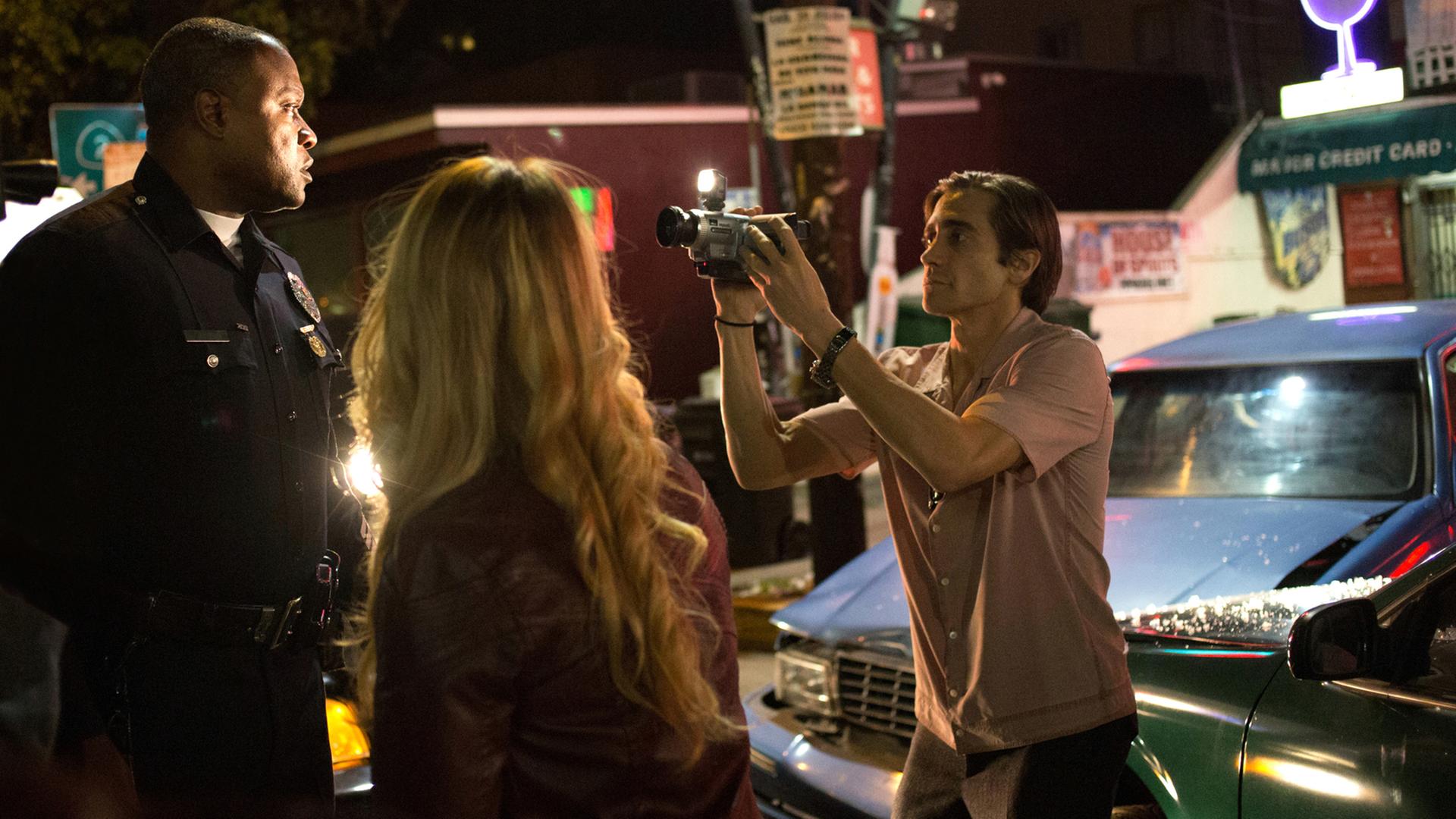 Die Szene des Films "Nightcrawler - Jede Nacht hat ihren Preis" zeigt den Kameramann Lou (Jake Gyllenhaal, r.) bei seiner rücksichtslosen Aufnahme eines Ereignisses auf der Straße.