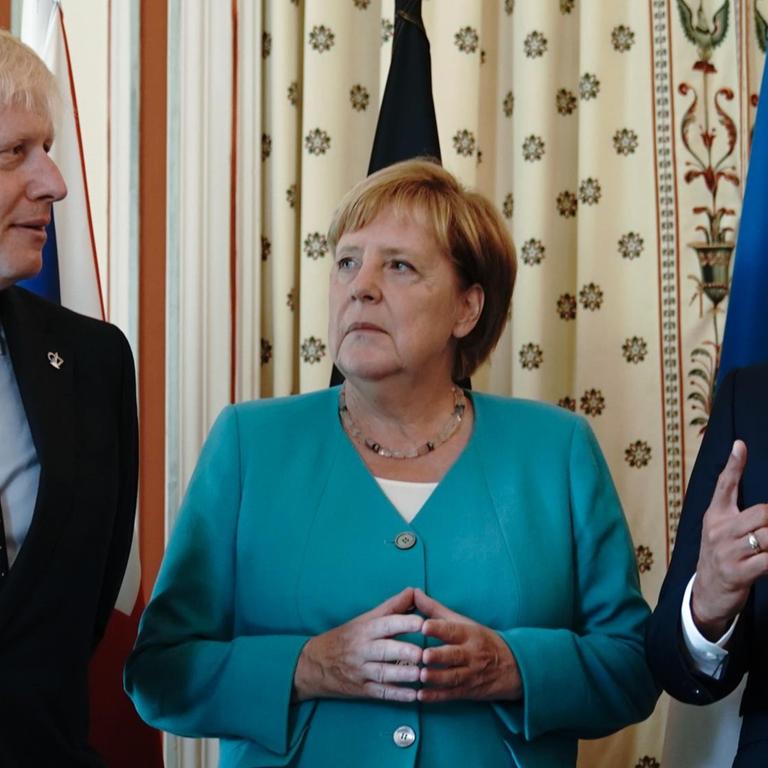 24.08.2019, Frankreich, Biarritz: Bundeskanzlerin Angela Merkel (CDU), steht zwischen Boris Johnson (l), Premierminister von Großbritannien, und Emmanuel Macron, Präsident von Frankreich