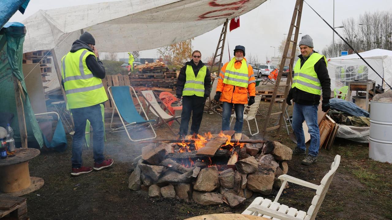 30.11.2018, Frankreich, Bernolsheim: Vier "Gelbwesten" wärmen sich in ihrem Protestcamp nahe Straßburg an einem Lagerfeuer.