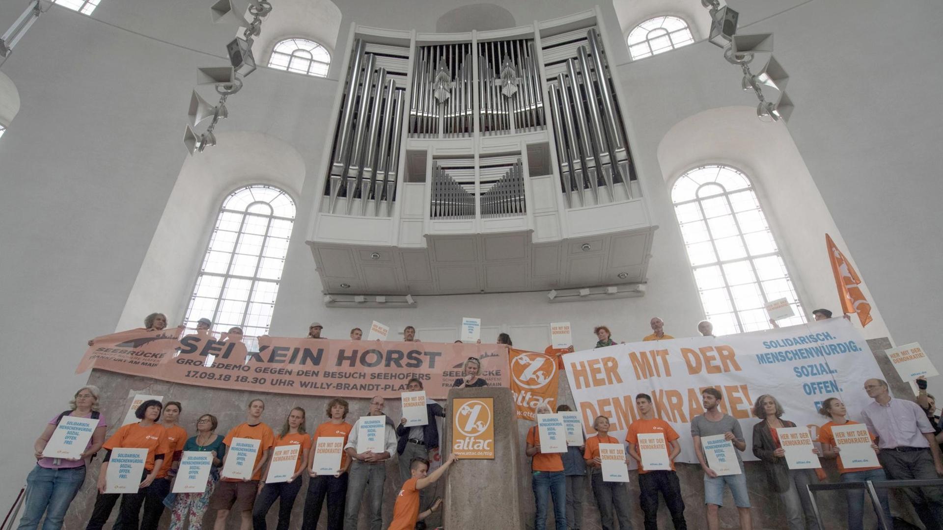 Attac-Aktivisten halten vor der Orgel in der Paulskirche Plakate in die Luft.