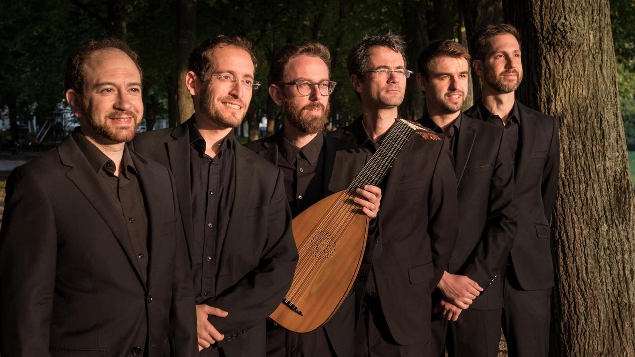 Sechs Musiker, einer mit Laute, von "Profeti della Quinta" stehen in einer Reihe neben einem großen, alten Baum.