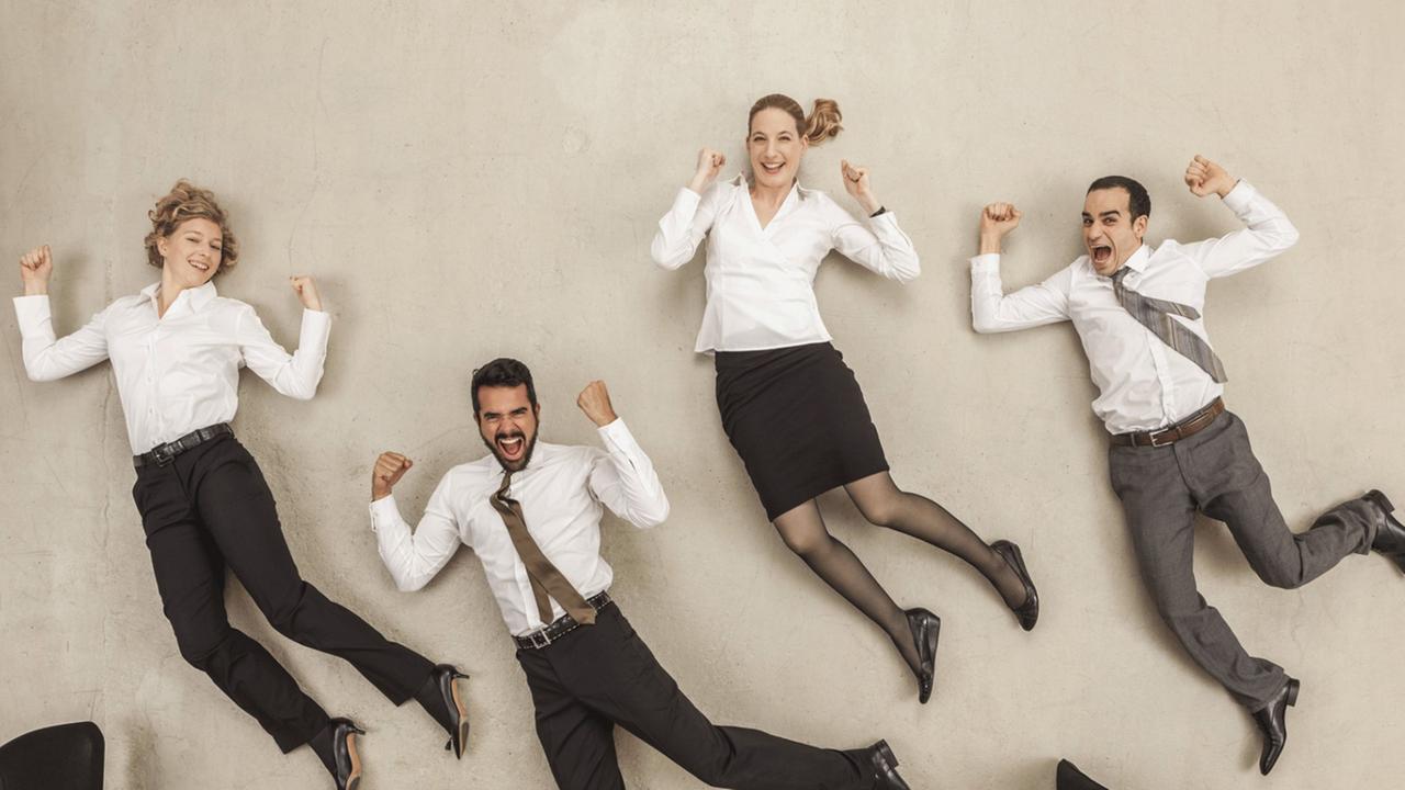 Menschen in Businesskleidung liegen auf dem Rücken, als würden sie durchs Büro springen