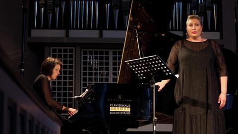 Eine Sängerin steht vor einem großen Konzertflügel, am Instrument sitzt eine Pianistin.