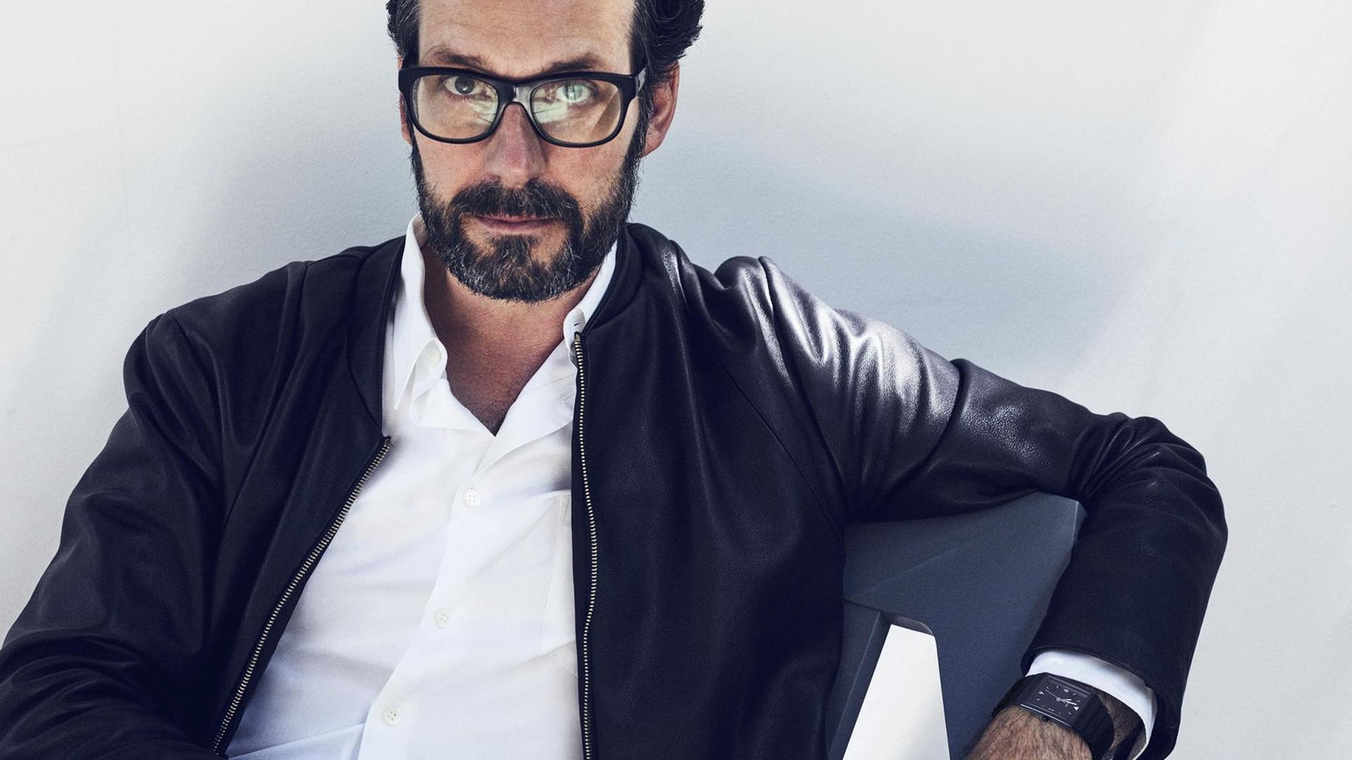 Porträt des Industrie-Designers Konstantin Cricic. Er trägt eine schwarze Lederjacke und sitzt in einem von ihm entworfenen Stuhl vor weißem Hintergrund.
