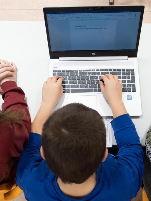 Schüler einer 3. Klasse sitzen in einem Klassenzimmer vor einem Laptop.