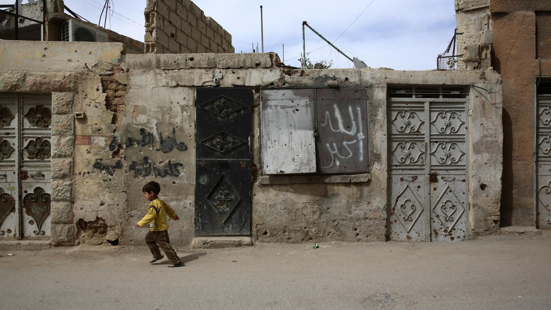 Ein Junge läuft in einem Vorort von Damaskus in Syrien an zerstörte Häuser vorbei.