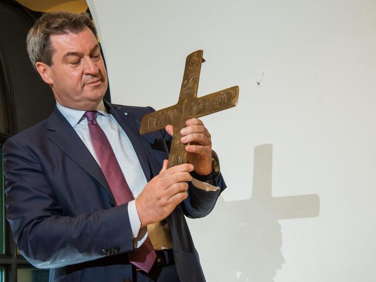 Der bayerische Ministerpräsident Markus Söder hält ein Kreuz