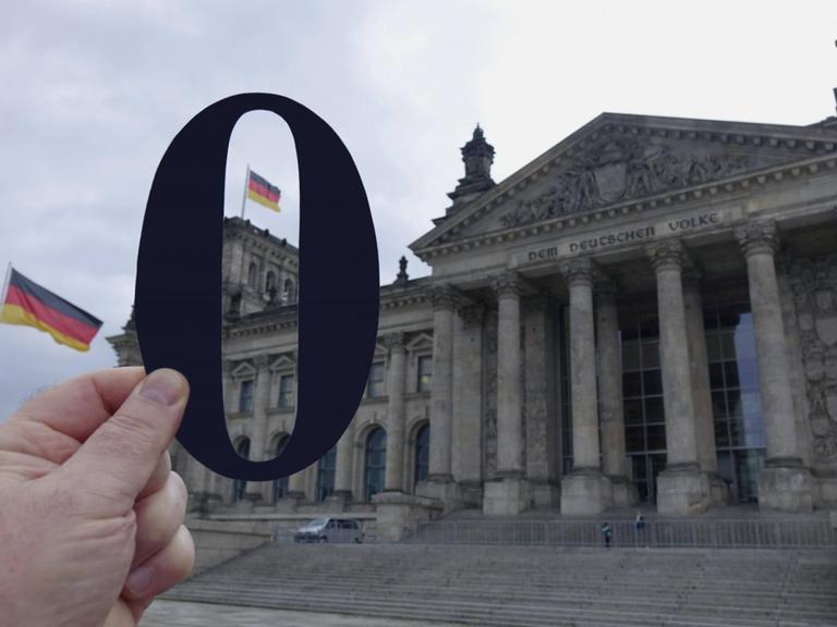 Eine Hand Hält eine ausgeschnittene schwarze Null vor den Reichstag.