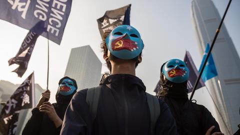 Schwarzgekleidete Demonstranten tragen blaue Gesichtsmasken. Darauf gemalt sind Hände mit einer chinesischen Flagge in Form einer Hand, die den Mund zuhält.