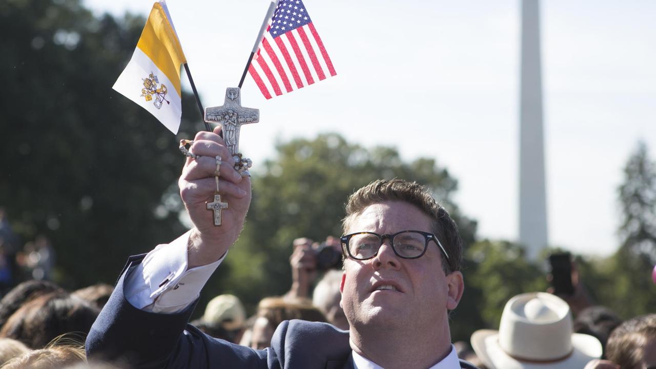 Ein weißer US-Amerikaner hält während des Papstbesuchs in den USA im September 2015 die amerikanische und die Flagge des Kirchenstaats in den Händen 