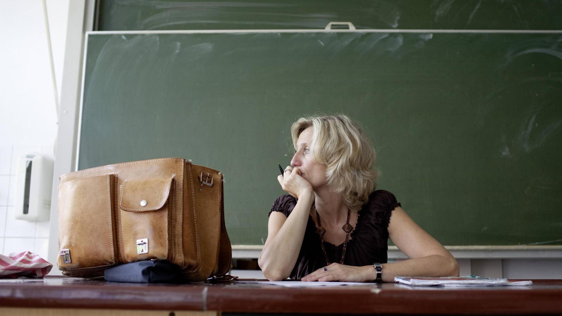 Eine Lehrerin sitzt vor einer leeren Tafel und schaut aus dem Fenster