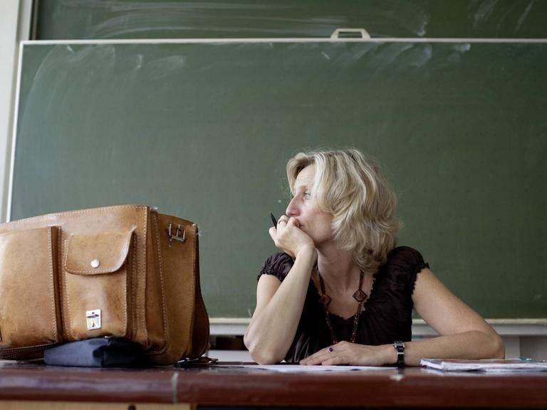 Eine Lehrerin sitzt vor einer leeren Tafel und schaut aus dem Fenster